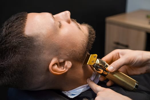 Barber shearing beard to man in barbershop, close up.