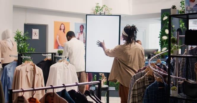 Man in shopping center fashion boutique using high tech screen to look at clothes options to try on. Client using led panel to visualize outfit combinations in store before buying, ground level shot