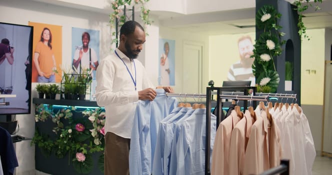 BIPOC man restocking luxurious clothing store with elegant assortment of blazers. African american worker arriving with new stylish attire garments from new collection in premium fashion boutique