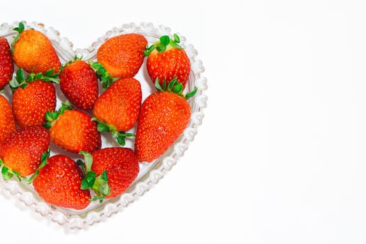 A bunch of fresh strawberries in a heart shaped bowl on a white Background.