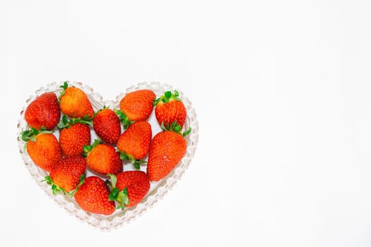 A bunch of fresh strawberries in a heart shaped bowl on a white Background.