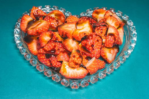 Peaces of strawberries in a heart shaped bowl on a blue background.