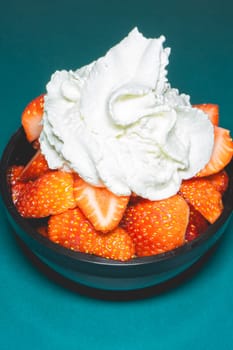 A bowl with fresh strawberries with Whipped cream on a blue background.
