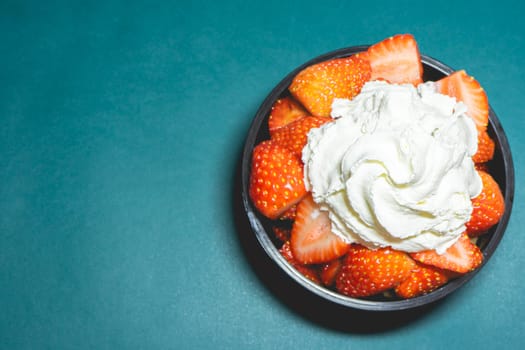 A bowl with fresh strawberries with Whipped cream on a blue background.