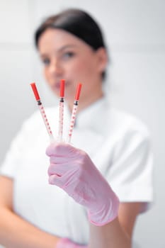 Blurry portrait of cosmetologist woman holding three syringes in hand. The concept of professional rejuvenating skin care. Female dermatologist showing injections in beauty clinic.
