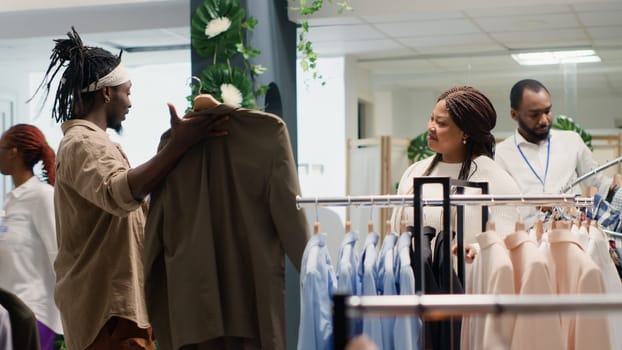 Shopper in luxurious clothing store asking girlfriend to pick between two elegant shirts. Trendy customer looking for clothes in premium fashion boutique, handheld camera shot