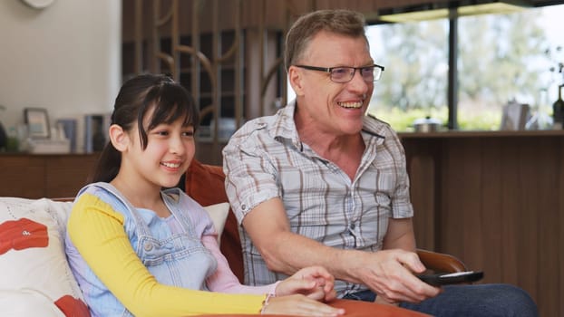 Grandfather and granddaughter together watch interesting entertainment media on TV. Old senior use technology communicate with young generation cross generation gap strengthen family bond. Divergence.