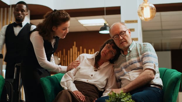 Elderly people sleeping on each other at hotel reception, waiting to see room reservation and start holiday. Retired exhausted couple dealing with jetlag after international flight. Handheld shot.