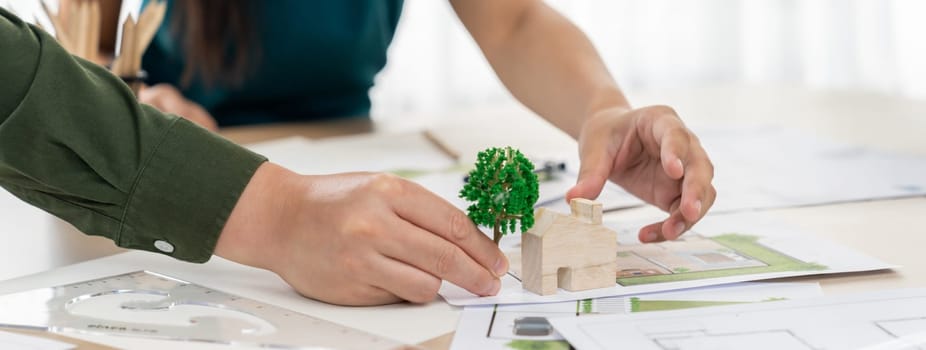 Professional architect team discuss about green design of eco house on meeting table with blueprint and model scatter around. Closeup. Focus on hand. Green city concept. Delineation.