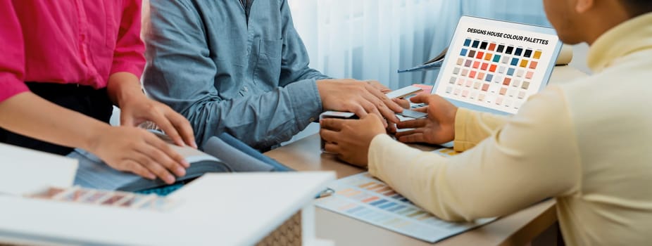 Professional architect presents color selection by using laptop displayed the color while female interior designer selects the curtain material. Creative working and teamwork concept. Variegated.