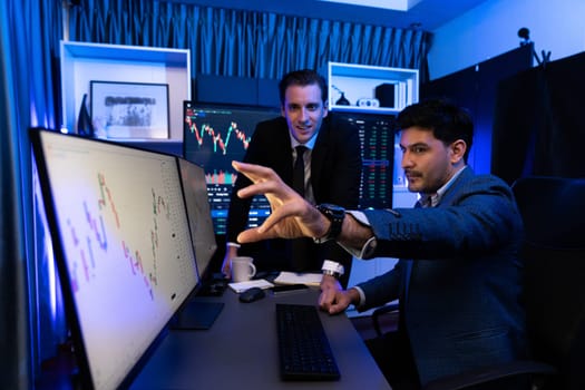 Two stock investors discussing and pointing interesting market stock on monitor. Trend of the technology for dynamic economic investment for planning to select at neon light workplace. Sellable.