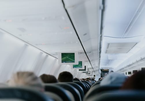 View of an electronic board with a flight path, inside a flying airplane with unrecognizable people sitting with their backs in chairs, close-up side view.