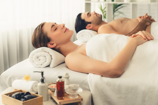 Caucasian couple customer enjoying relaxing anti-stress spa massage and pampering with beauty skin recreation leisure in day light ambient salon spa at luxury resort or hotel. Quiescent