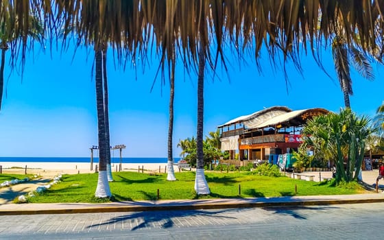 Typical beautiful colorful tourist street road and sidewalk at coast beach with city life cars traffic buildings hotels bars restaurants and people in Zicatela Mexico.