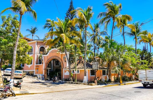 Typical beautiful colorful tourist street road and sidewalk with city life cars traffic buildings hotels bars restaurants and people in Zicatela Mexico.