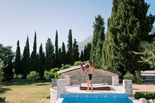 Man holds woman on his shoulder while standing on the edge of the pool near a sun lounger. High quality photo