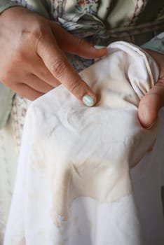 women holding white color dirty shirt, showing making stain.