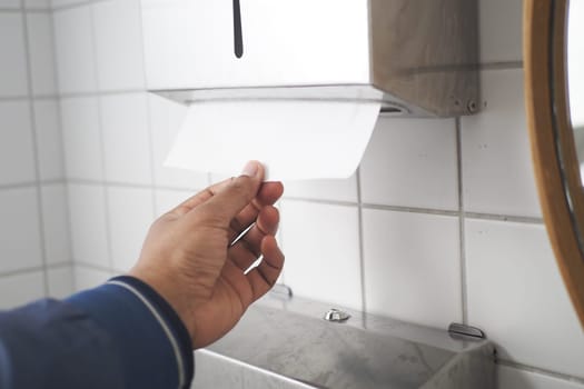 A person is using a paper towel dispenser in a public restroom,