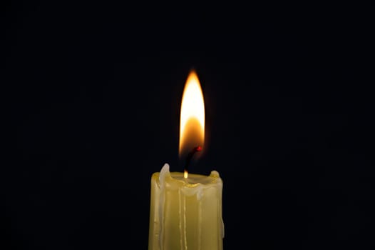 Burning yellow wax candle contrasting with the dark background, candle's gentle flame suggesting of remembrance, reflection and hope