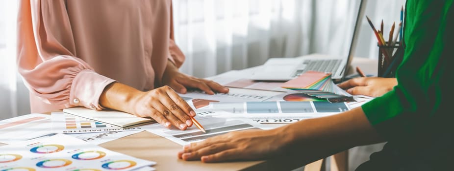 Cropped image of professional interior designers discuss and brainstorm main theme color in project on meeting table with color palette scatter around. Creative interior design concept. Variegated.