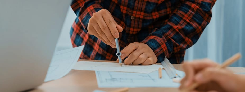 A professional engineer uses divider to measure blueprint during skilled architect drawing blueprint at architectural project meeting. Teamwork and cooperation concept. Closeup. Delineation.