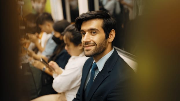 Smiling caucasian business man looking at mobile phone or playing social media while sitting in train. Attractive project manager going to work place by using public transport in rush hour. Exultant.