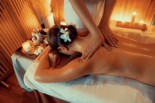 Caucasian woman customer enjoying relaxing anti-stress spa massage and pampering with beauty skin recreation leisure in warm candle lighting ambient salon spa at luxury resort or hotel. Quiescent