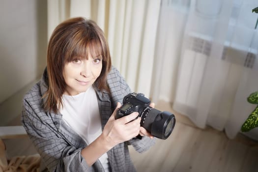 Senior old elderly woman with black camera with a large lens indoors in the studio. Professional photographer. Age Hobby