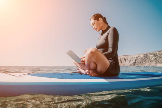 Digital nomad, woman in the hat, a business woman with a laptop sits on the rocks by the sea during sunset, makes a business transaction online from a distance. Freelance, remote work on vacation.