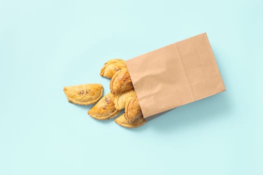 Delightful Food Delivery: Samsa Pies Sprinkled with Poppy Seeds in Paper Bag on Blue Background.