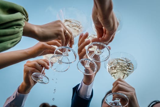 Group of people clinking glasses with martini against the sky during party summer outdoor, closeup.