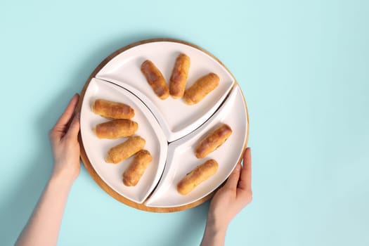 Woman's Hands Holding a Plate of Sweet Delights for Tea: Top-Down View of Croissants, Sweet Rolls, or Twisted Cookies.