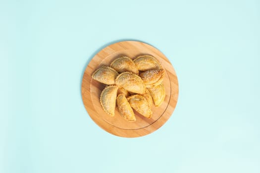 Top view baked samosa pies with chicken sprinkled with sesame seeds on wooden plate on blue background, central asian street food.