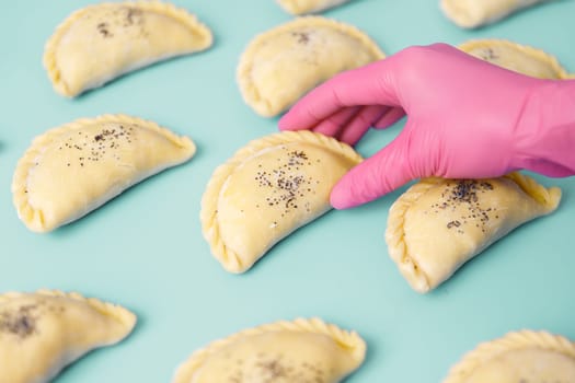 A baker's hand in a rubber glove lays out raw samosa on the table. Traditional Central Asian cuisine, frozen semi-finished products.