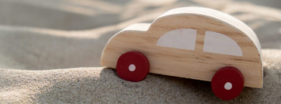 Wooden toy car on sandy beach background. Eco-friendly travel, reduce carbon footprints, environmental impact, Conscious Traveler, Environmentally Friendly, responsible traveler Eco-car concept World car free day. Roadtrip local travel