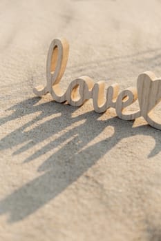 Wooden word love on sandy beach background. Concept of romantic holiday anniversary, proposal, valentines day greeting card, postcard. Letter text in tropical vacation Sand surface. Deep shadows Love is all you need