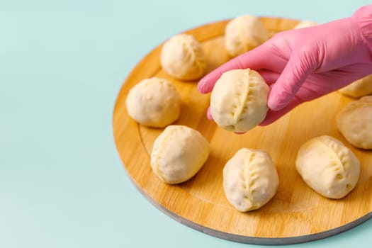 Close-up of a skilled chef's hand in a rubber glove holding a single traditional Central Asian manty, surrounded by frozen semi-finished products, copy space.