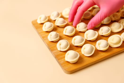 A chef's hand in a rubber glove carefully lays out semi-cooked raw dumplings on a wooden board, copy space.
