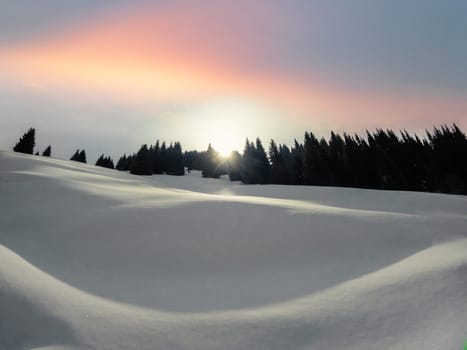 Dawn in the winter mountains of Central Asia. The morning sun peeks out from behind the mountain, illuminating the snow-covered slope.