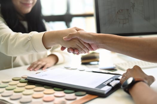 Smiling female client shaking hands with Interior designer after signing agreement.