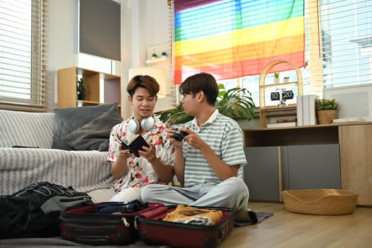 Young gay couple packing cloth and stuff for vacation trip in the living room at home.