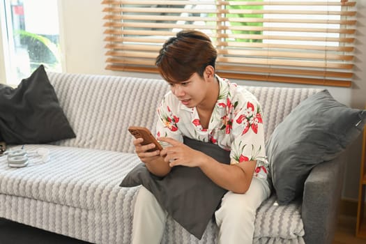 Happy smiling casual man using smart phone relaxing on sofa at home.