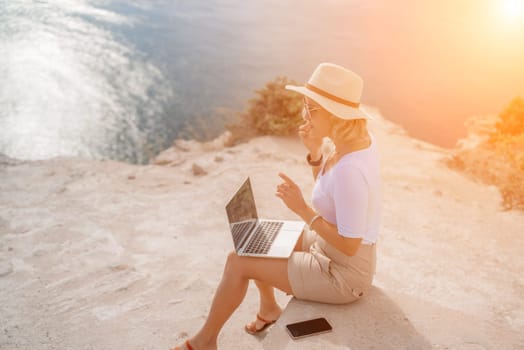 Freelance women sea working on the computer. Good looking middle aged woman typing on a laptop keyboard outdoors with a beautiful sea view. The concept of remote work