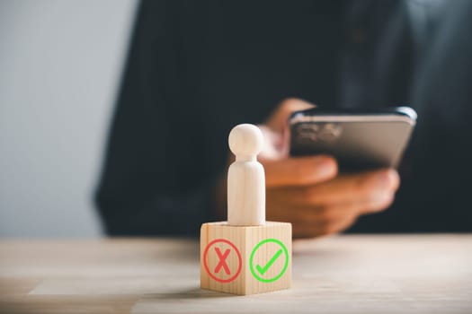 Businessman using smartphones selects right or wrong symbols on wooden block for a yes or no decision-making. Communication of choice and progress. Think With Yes Or No Choice.
