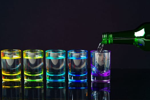 Colorful small glasses on black background with alcohol drink close up
