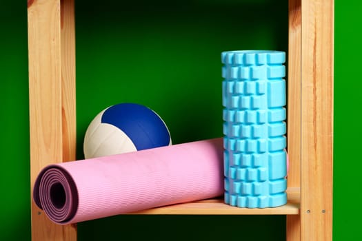 Shelves with different sports equipment against green wall close up