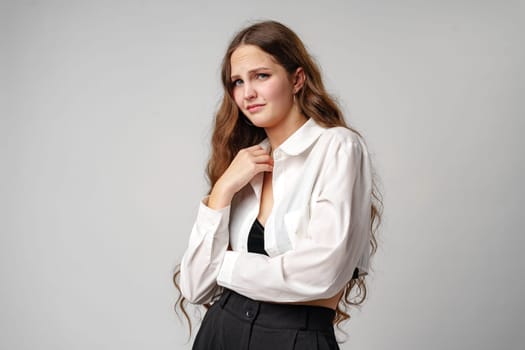 A woman stands wearing a white shirt and black pants. She is posing for the camera in a casual outfit, exuding confidence and style.