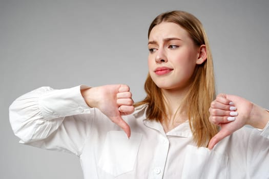 Young Woman in White Shirt Pointing Finger Down Dislike against gray background