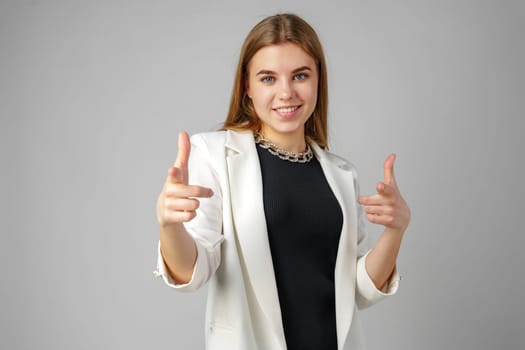 Young Woman in White Blazer Pointing at You Against a Grey Background in Studio