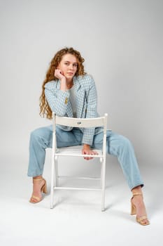 Young woman with curly hair sitting on chair in studio close up